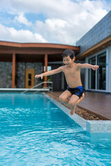 Asian Young Boy Having a good time in swimming pool, He Jumping and Playing a Water in Summer.