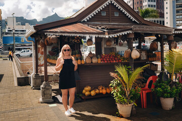 A tourist girl stands near a fruit counter in Port Louis, Mauritius - obrazy, fototapety, plakaty