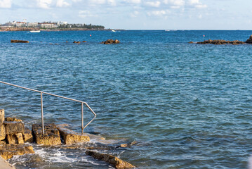 Naklejka premium Descent into the sea from stone steps. Turquoise sea at the waterfront of the city of Paphos in Cyprus in autumn.