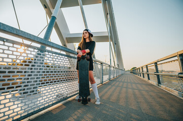Young woman holding her longboard and standing on the bridge