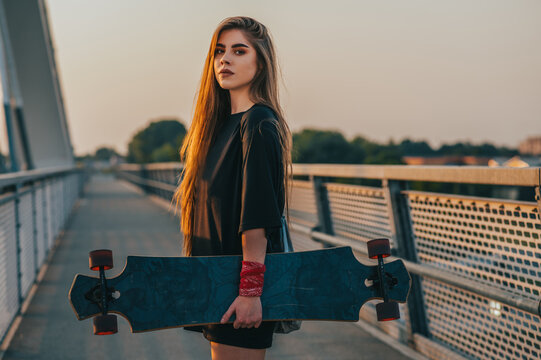 Young woman holding her skateboard and standing on the bridgeYoung woman holding her longboard and standing on the bridge