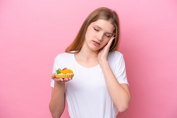 Teenager Russian girl holding a tartlet isolated on pink background with headache