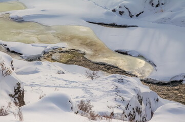 Winter landscape with a fast river with ice-free water, snow and a stone bank