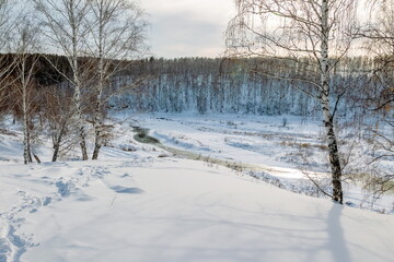 Winter landscape with birches, river, snow and blue sky with clouds