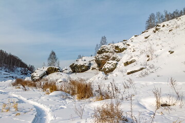 Fototapeta na wymiar Winter landscape with a rocky riverbank, dry grass, trees against a blue sky background