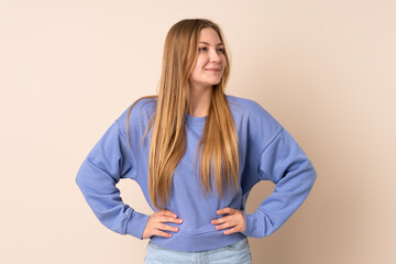 Fototapeta premium Teenager Ukrainian girl isolated on beige background posing with arms at hip and smiling