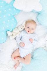 happy baby boy six months old lying on the bed with a stuffed toy bunny, cute blonde baby