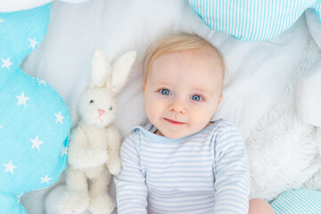 portrait of a happy baby boy six months old on a bed, cute blonde baby