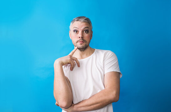 A Gay Man With Makeup In A White T-shirt On A Blue Background Looking At The Camera.