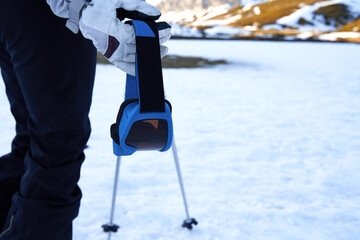 close-up of ski goggles held by a hand equipped with a snow glove.