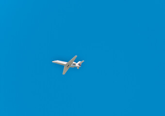 bottom view, very far distance of a private, twin, passenger jet, with a blue sky background