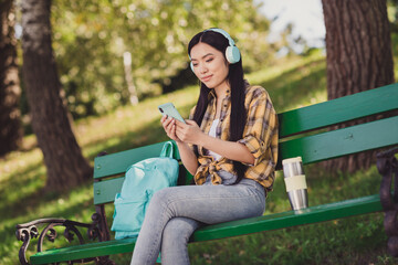 Photo of shiny charming young woman dressed plaid shirt sitting bench listening good music modern device smiling outside countryside nature