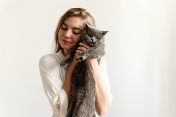 a sexy girl in thin pajamas sits on the bed and holds a beautiful Scottish cat. sexy girl at home in pajamas on a bed with a pet