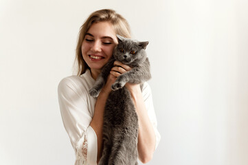 a sexy girl in thin pajamas sits on the bed and holds a beautiful Scottish cat. sexy girl at home in pajamas on a bed with a pet