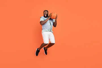 Photo of excited funny afro guy wear denim vest holding ball jumping high isolated orange color background