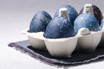 Blue easter eggs dyed with hibiscus tea in an egg carton on a white concrete background
