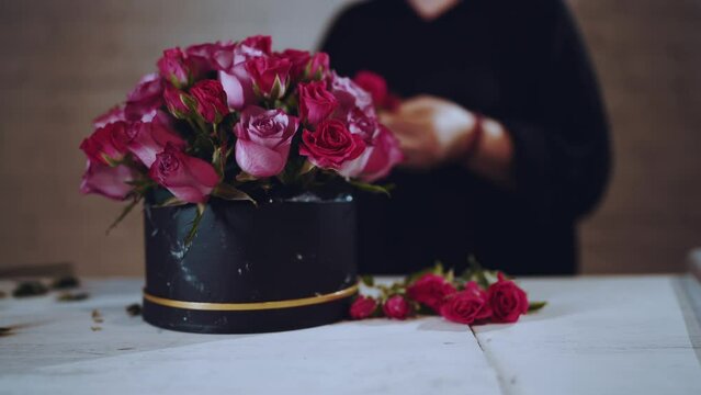 Florist collects a bouquet of roses, a hatbox with flowers of roses