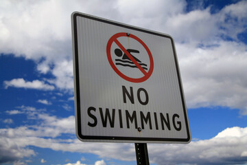The No Swimming sign with the icon and a blue and white sky behind