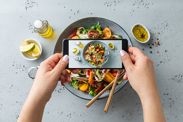 Woman taking photo of vegetable salad with smartphone. Posting food pictures (images) on social media.