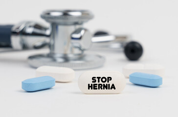 Obraz na płótnie Canvas On a white surface lie pills, a stethoscope and a tablet with the inscription - STOP HERNIA