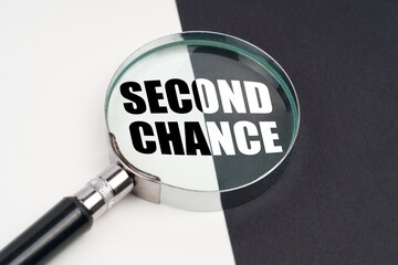 On the surface, which is half black and white, lies a magnifying glass inside which is written - SECOND CHANCE