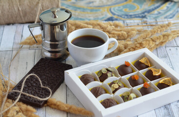 Handmade candies and coffee in a porcelain cup and heart with a rope on a chocolate bar on a gray wooden background.