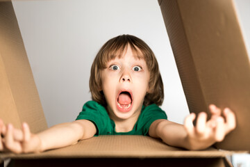 Funny little boy jumping with scary face jumping out of the cardboard box.