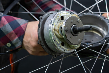 Repair of electric bicycles. A bicycle mechanic holds a wheel with an electric motor and a wrench in his hands. Bicycle wheel close-up on a black background.