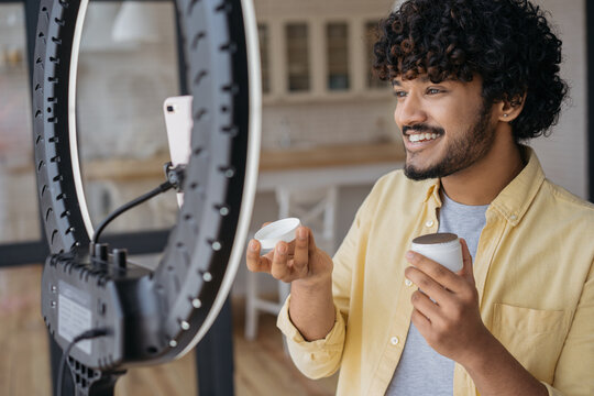 Smiling successful Indian blogger influencer recording video communication online with subscribers holding cream, talking about skin product