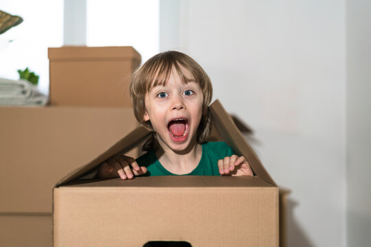 Excited little boy jumping inside a huge cardboard box. He is playing and looking out of a box. Kid is happy about moving into a new home.
