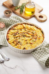 Slices potato casserole with red onions, fresh thyme and rosemary on green checkered kitchen towel , wooden board with flavoring ingredients: pepper, salt, olive oil