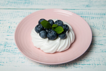 Pavlova cake with blueberries and mint on a pink platter. Home confectionery. Old retro white and blue table.