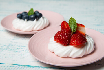 Pavlova cake with strawberries and blueberries and mint on a pink platter. Home confectionery. Old retro white and blue table.