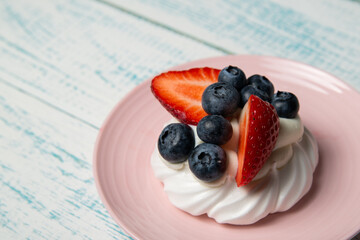 Pavlova cake with strawberries and blueberries on a pink platter. Home confectionery. Old retro white and blue table.