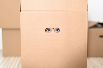Boy hiding in inside a huge cardboard box. He is playing and peeking through a hole in box. Kid is happy about moving into a new home.