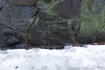 Stone wall with white melting snow at the foot