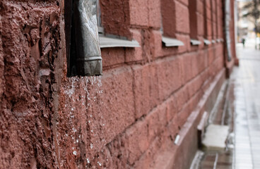 Water flowing from drain pipe on blurred background of a city street