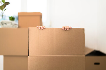 Excited little boy hiding inside a huge cardboard box. He is playing and going to jump out of the box. Kid is happy about moving into a new home.