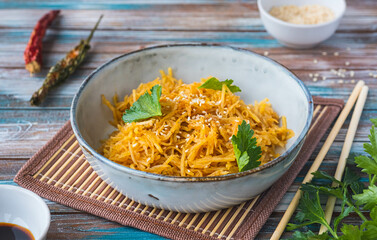 Korean spicy potato salad sprinkled with sesame seeds in a gray ceramic bowl on a wooden background. Salad recipes.