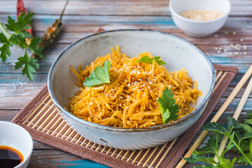 Korean spicy potato salad sprinkled with sesame seeds in a gray ceramic bowl on a wooden background. Salad recipes.