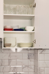 Fototapeta na wymiar Open white kitchen cabinet door with white dishes inside