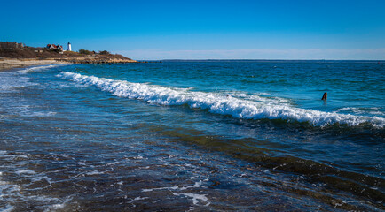 White waves rolling in diagonally on the rocky beach at Knobska Lighthouse beach on Cape Cod.