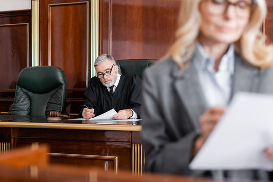 senior judge reading lawsuit near attorney on blurred foreground