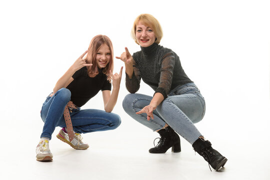 Mother and daughter teenager knelt down and cheerfully show youth gestures in the frame