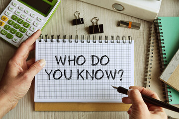 The inscription in the notebook WHO DO YOU KNOW. Top view of the desktop. In the frame are the hands of a young girl, a calculator, office supplies. 