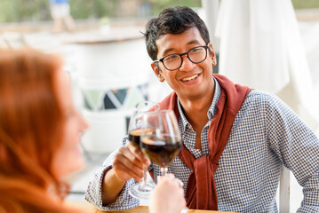 Cheerful Asian man drinking wine with friends in restaurant