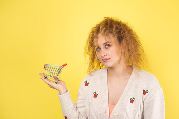 A young beautiful curly red-haired girl holds a food cart in her hands. Shopping concept.