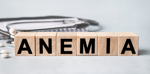 ANEMIA inscription on wooden cubes isolated on white background, medicine concept. Nearby on the table are a stethoscope and pills.