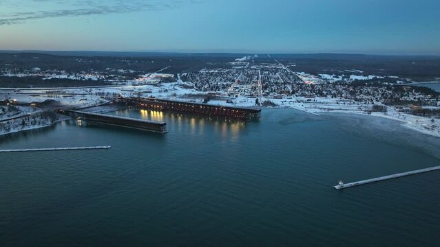 Two Harbors, Minnesota Aerial Footage - Drone  video of snowy town on lake shore at dusk with lighthouse and loadings docks