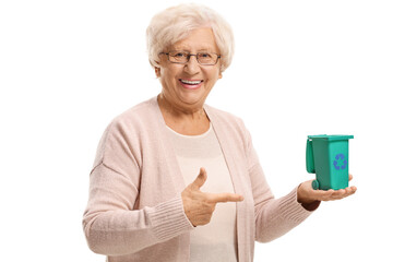 Smiling elderly woman holding a small recycling bin on her hand and pointing